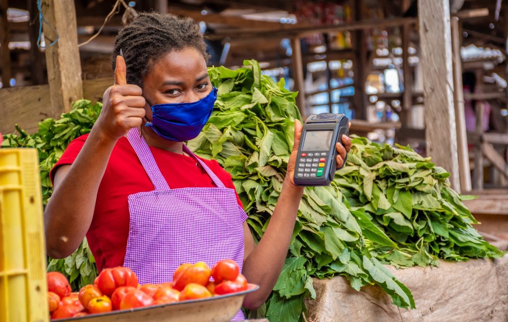 A shallow focus of an African female with a facemask holding a POS machine at a market