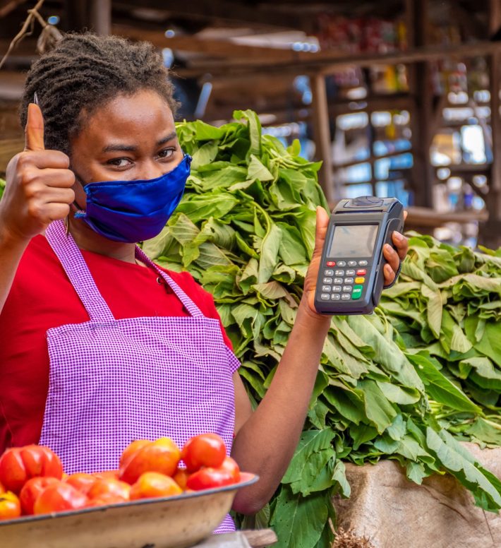 Shallow focus of an African female with a facemask holding a POS machine at a market A shallow focus of an African female with a facemask holding a POS machine at a market