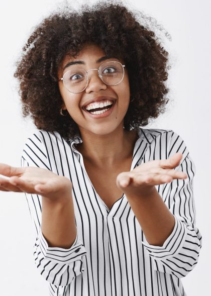 Woman retelling exciting story with emotive gestures. Thrilled and amazed african-american talkative woman with curly hair in glasses and striped blouse raising palms near chest as if holding item Woman retelling exciting story with emotive gestures. Thrilled and amazed african-american talkative woman with curly hair in glasses and striped blouse raising palms near chest as if holding item.